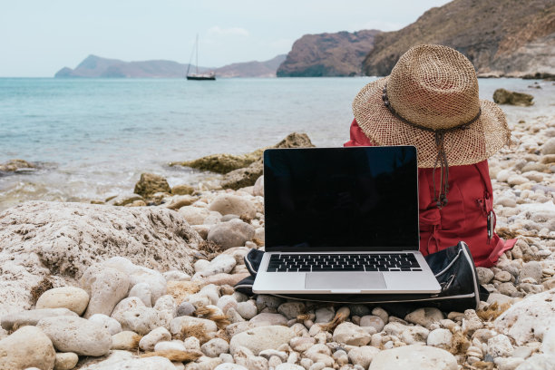 红色冒险和旅行双肩包，带着一顶草编沙滩帽，还有一台在地中海前打开屏幕的笔记本电脑。度假概念和目的地旅游和远程工作图片下载