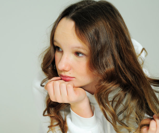 十几岁的女孩穿着白色卫衣在画室的白色背景上站着各种鬼脸，她是美丽的和年轻的图片下载