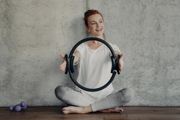 快乐微笑的红发女人坐在莲花姿势与普拉提环在锻炼图片下载