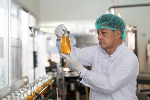 在饮料厂的传送带上，亚洲男性工人正在检查产品瓶罗勒种子和水果。制造商在饮料厂检查。检验质量控制图片下载