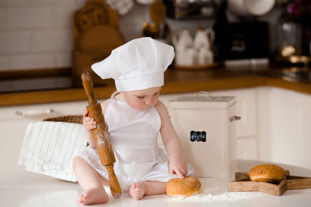 孩子们的厨师。漂亮的小男孩，围着白围裙，戴着厨师帽，手里拿着搅拌器。背景是厨房的内部。烹饪概念。图片下载