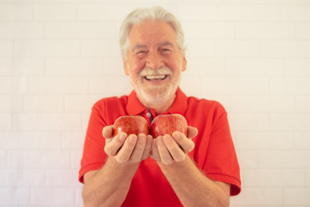 分散的微笑的高级男子在红色孤立在一个白色的背景，手里拿着两个红色的苹果水果看相机-健康的饮食概念图片下载