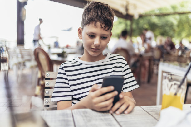 男孩沉迷于户外网络游戏。男孩使用手机和玩游戏。图片下载
