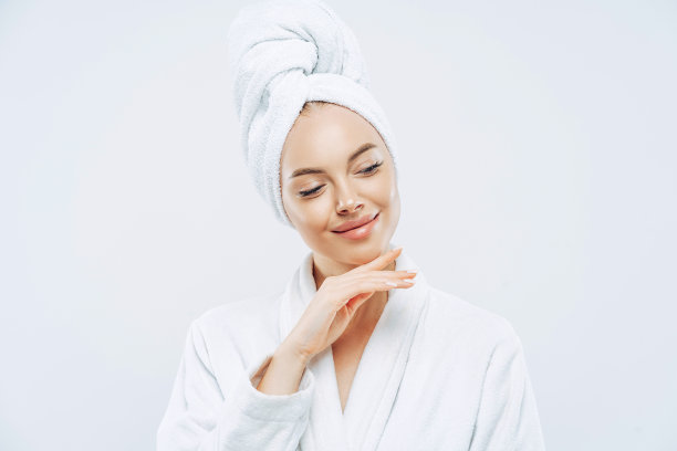 漂亮自然的女人轻轻触碰下颚，用浴巾包裹头部，淋浴后吹干头发，关心身体，皮肤干净，准备参加晚会，穿着家庭长袍图片下载