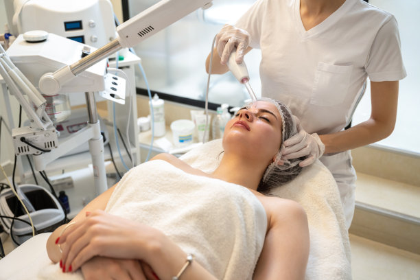美容院的美容师在女性患者的额头上使用特殊工具进行电动达索瓦面部按摩图片下载