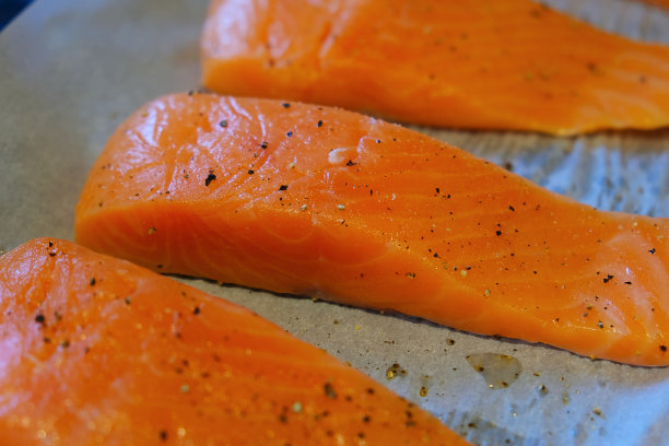 新鲜生三文鱼鱼片与盐和胡椒在烤纸上准备烤或烧烤食物的背景特写照片与拷贝空间。野生捕获的大西洋挪威鱼图片下载