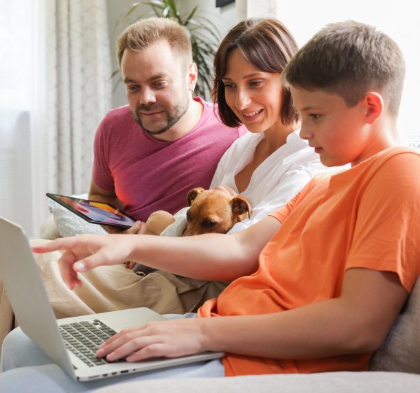 家里的沙发上放着平板电脑和笔记本电脑。妈妈，爸爸和儿子一起在家使用笔记本电脑平板电脑。网上购物、网上冲浪、视频叫网络游戏的概念。图片下载