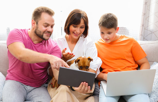 家里的沙发上放着平板电脑和笔记本电脑。妈妈，爸爸和儿子一起在家使用笔记本电脑平板电脑。网上购物、网上冲浪、视频叫网络游戏的概念。图片下载