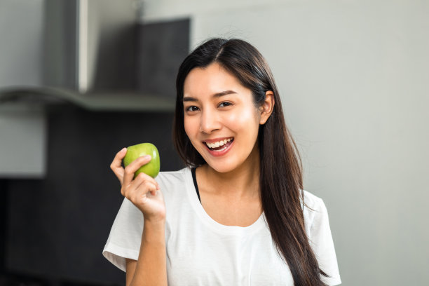 年轻女性在减肥饮食和健康餐桌上吃绿色苹果。美丽的女人早上在厨房愉快地吃着健康的沙拉早餐。减肥食品的概念。图片下载
