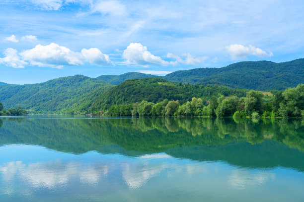 河岸被森林覆盖，水中倒映着云朵图片下载