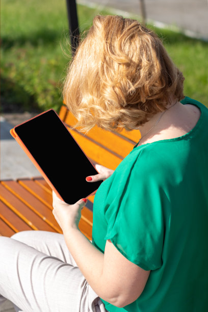 一名女商人戴着墨镜的肖像，手里拿着一台现代数码平板电脑，坐在街上的长凳上。图片下载