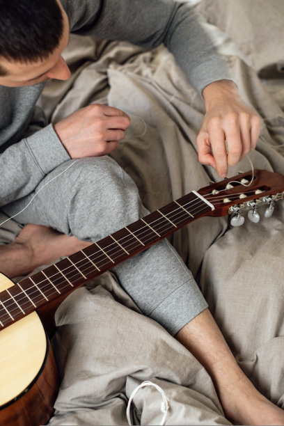 年轻人坐在家里的床上换原声吉他弦图片下载