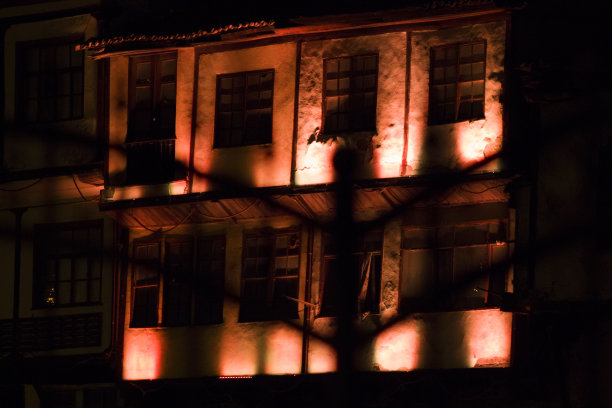 晚上黑栏杆后面的老房子。古老的豪宅被红光照亮。专注于老房子图片下载