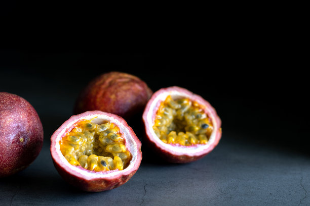 深色背景上的完整和切半的新鲜多汁百香果，留白区域。异国情调水果的背景。图片下载