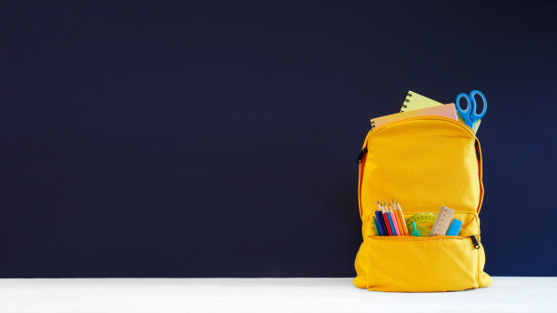 桌子和蓝色背景上装有彩色文具的背包，返校季banner设计，蓝色黑板图片下载