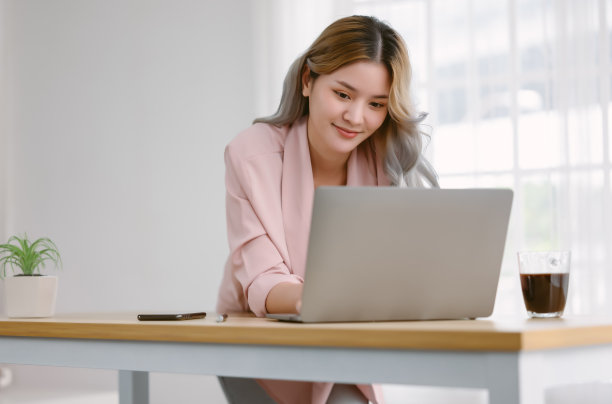 微笑美丽的亚洲女人使用笔记本电脑放松休闲的工作，而站在书桌。年轻时尚有创意的日本或韩国女孩工作交流在线。在家工作的概念。图片下载