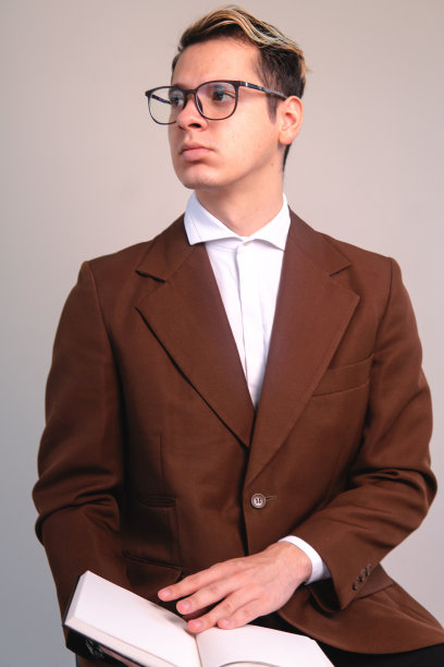 一个优雅的男人看着某样东西。男人与反思姿势。优雅的男子在白色背景前摆姿势。时髦的男人手里拿着一本书。图片下载