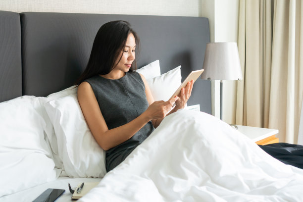 微笑的亚洲女商人工作在床上的平板电脑在酒店。商务旅行，人与科技，自由生活理念，文案空间图片下载