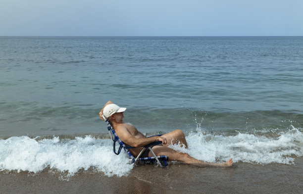上身赤裸的成年人泳装坐在沙滩上的椅子的侧面视图图片下载
