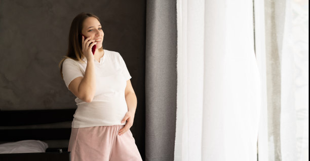 孕妇站在家里客厅用温暖的灯光、横幅讲手机图片下载