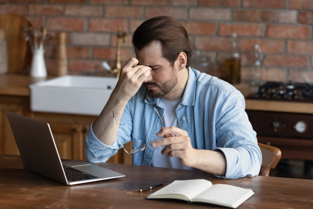 被笔记本电脑超负荷工作的男性自由职业者感觉不好，摘下眼镜图片下载