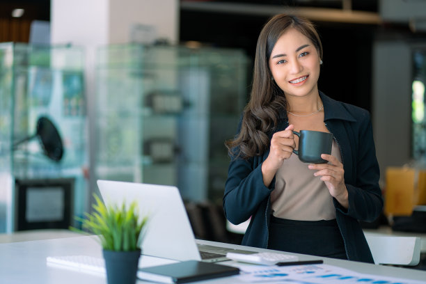 微笑美丽的亚洲女商人拿着咖啡杯和笔记本电脑在财务会计概念办公室用计算器分析图表图片下载