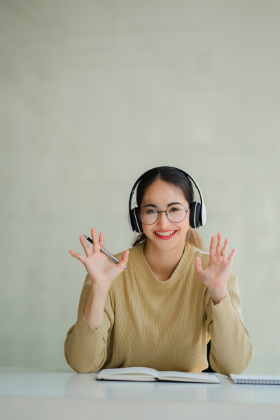 一名年轻的亚洲学生使用耳机和笔记本电脑在线学习，坐在家里的书桌前用笔记本做笔记。图片下载