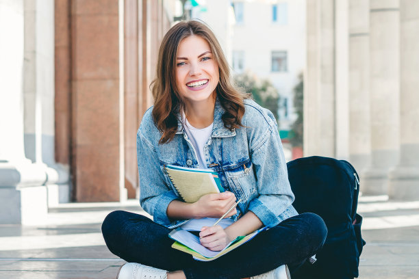 女学生坐在大学附近，微笑着。可爱的女学生拿着文件夹、笔记本大笑图片下载