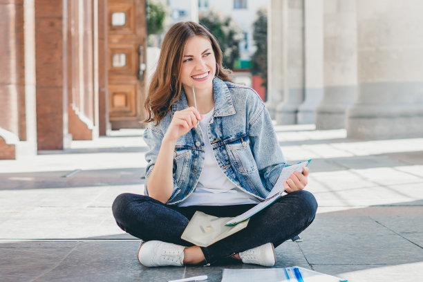 女生坐在学校对面，面带微笑。可爱的女学生拿着铅笔，文件夹，笔记本和笑。女孩教课程图片下载