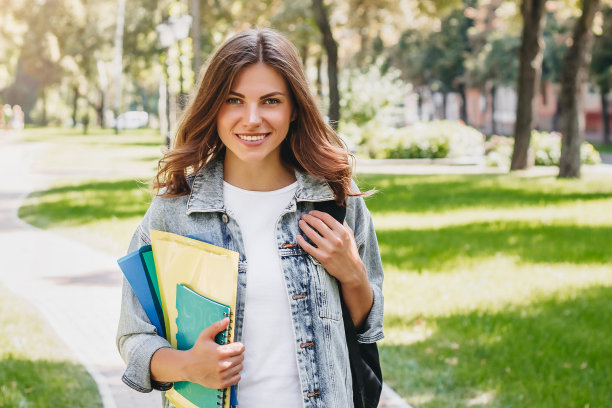 年轻的女学生在公园里微笑。可爱的女学生手里拿着文件夹和笔记本，复印空间图片下载