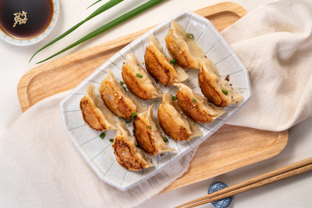 平底锅煎的日式饺子，配上酱油，放在白色的桌子上。图片下载