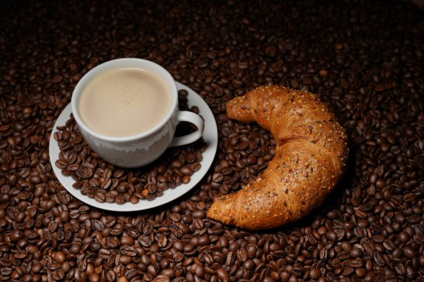 咖啡，咖啡杯，在咖啡豆上放一个牛角面包图片下载