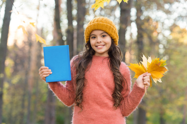 快乐的小朋友抱着学校的书在户外收集秋叶，畅想秋日图片下载