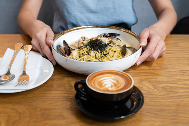 特写的女人的手拿海鲜意大利面与蛤蜊在白色盘子上的餐桌图片下载
