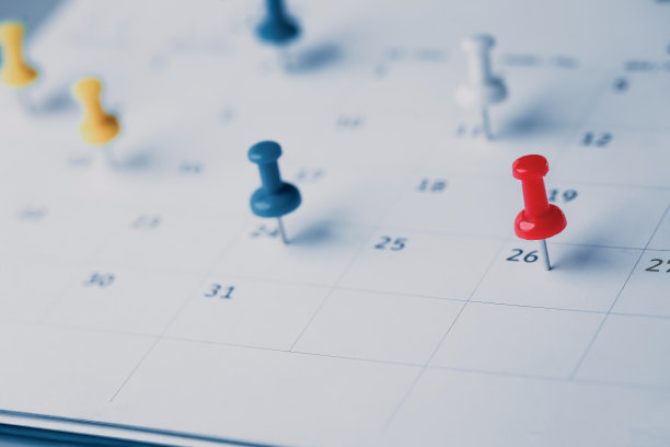 在日历上绣上红色大头针活动策划日历，以时钟设定时间表组织日程，策划商务会议或旅行计划的概念。图片下载