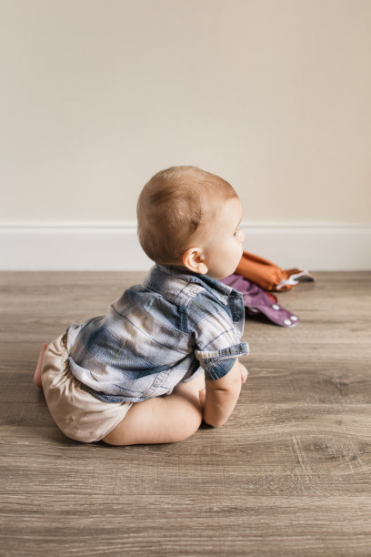 7个月大的多指畸形男孩穿着中性颜色可重复使用的布尿布学习一种新的发育技能:自己坐起来图片下载