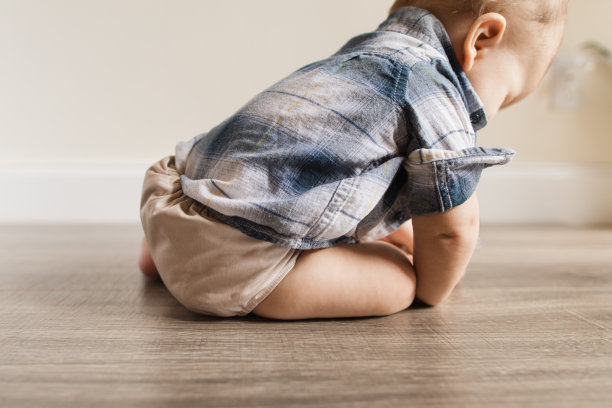 7个月大的多指畸形男孩穿着中性颜色可重复使用的布尿布学习一种新的发育技能:自己坐起来图片下载