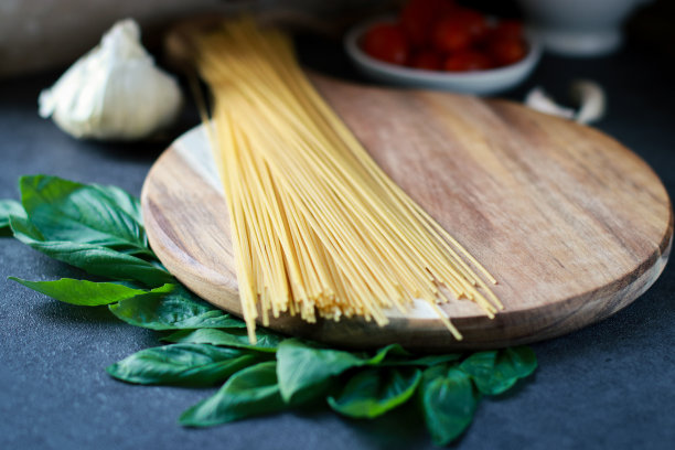 意大利面和帕尔马干酪在木板上的特写，模糊的背景与西红柿和大蒜图片下载