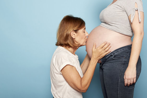 拉丁美洲祖母闭着眼睛亲吻孕妇的肚子。多代同堂家庭和怀孕理念图片下载