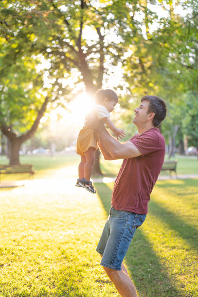 日落时分，一名男子抱着他一岁的小男孩在美丽的公园里图片下载