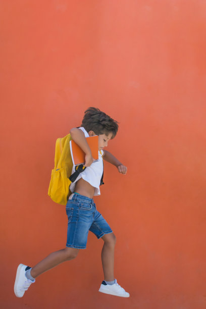 橙色背景下，男孩背着黄色背包，兴奋地跳着。图片下载