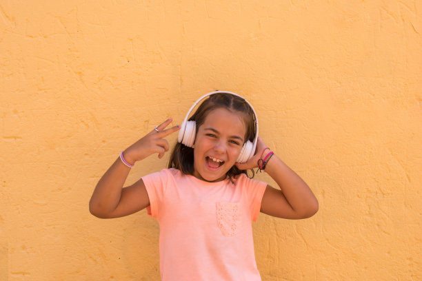 微笑的小女孩在上学年龄听音乐的无线耳机。图片下载