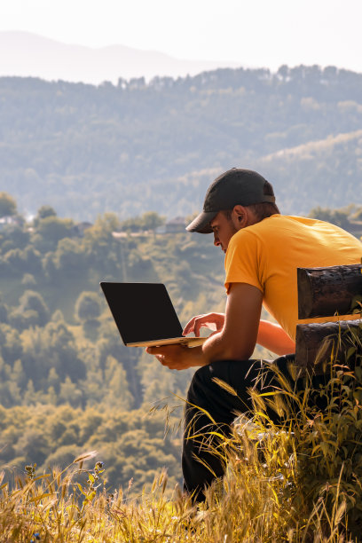 年轻的男性自由旅行者工作，学习在线户外，使用笔记本电脑，笔记本电脑在大自然的背景下，秋天的山林图片下载