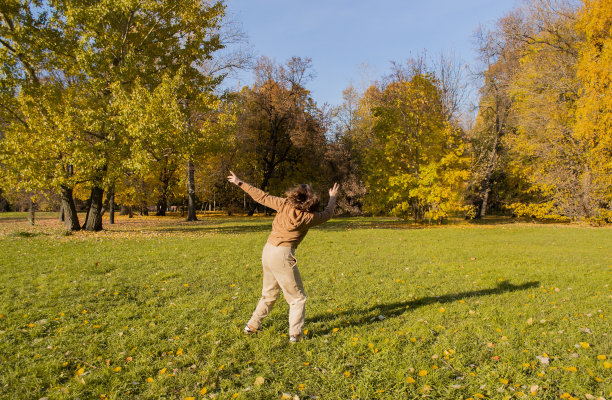 一个年轻女子在秋天的公园里享受自由。她跳来跳去，比划着图片下载