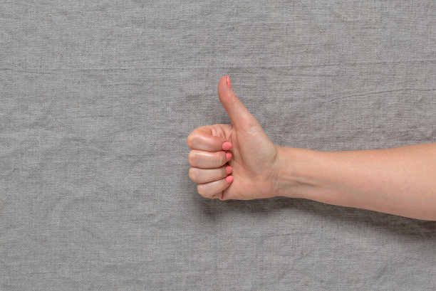 女人的手，大拇指朝上，纺织灰色的背景。图片下载