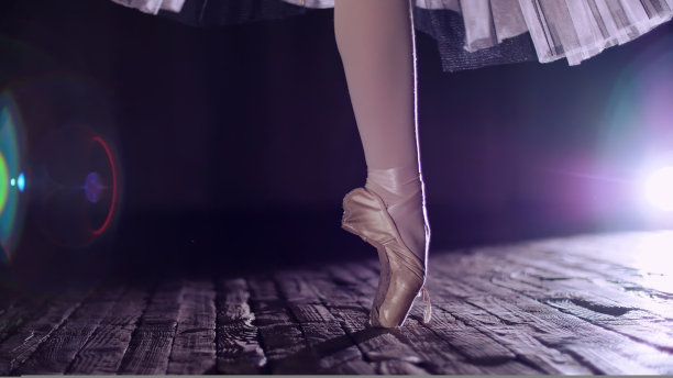 在聚光灯下，老剧院舞台上的特写。芭蕾舞女演员身穿白色芭蕾舞裙，穿着尖头鞋踮着脚尖旋转，优雅地表演一定的芭蕾舞动作、舞姿、足尖图片下载