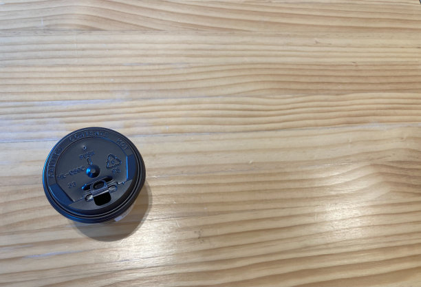 波浪图案的浅棕色木桌上放着一杯外卖的黑热咖啡图片下载