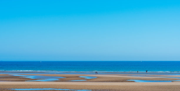 在晴朗的天空背景下，人们在海滩上散步，欣赏海景图片下载