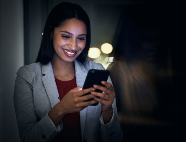 打电话打字，工作到很晚，和一位年轻的女商人一起加班到深夜，在她的办公室完成最后期限。快乐，积极，微笑的女性阅读或发送短信图片下载