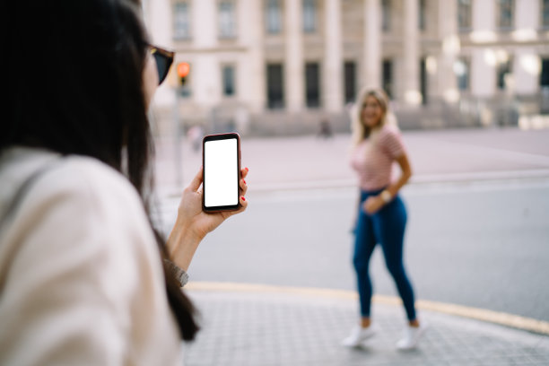 选择性集中在现代智能手机与模拟屏幕在womanâ的手，她最好的朋友，快乐的潮游客女性摆拍照片在城市目的地模糊的背景图片下载